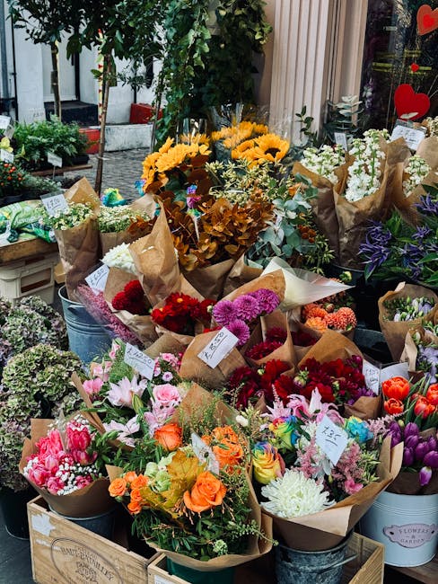 An outdoor display of fresh flower bouquets at a flower shop, featuring a variety of colourful arrangements wrapped in brown paper and placed in metal buckets and wooden crates. The bouquets include s