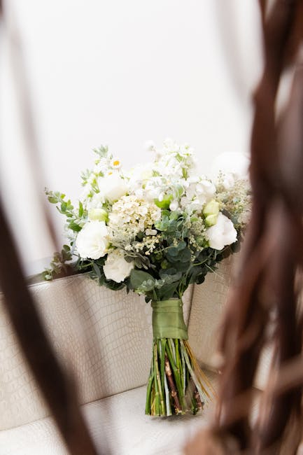 A bouquet of fresh white flowers, including roses, hydrangeas, and small filler blooms, accented with greenery such as eucalyptus leaves. The bouquet is arranged in a loose, natural style and is wrapp