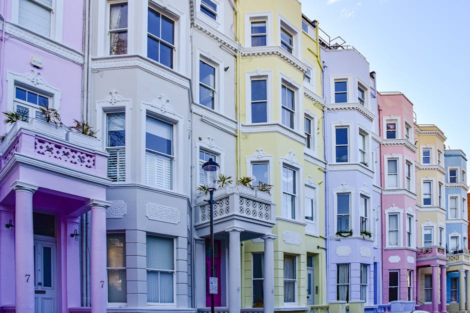 A row of colorful Victorian-style buildings in pastel shades of pink, yellow, green, and white, featuring decorative molding and bay windows. In the foreground, a classic black street lamp stands near