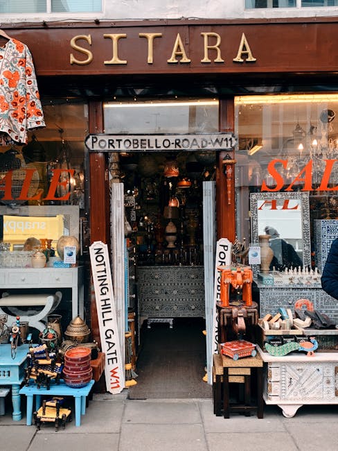 Photograph of the entrance to Sitara, a shop on Portobello Road in Notting Hill, featuring a wooden sign with the shop's name in gold lettering above the doorway. The shop displays a variety of items